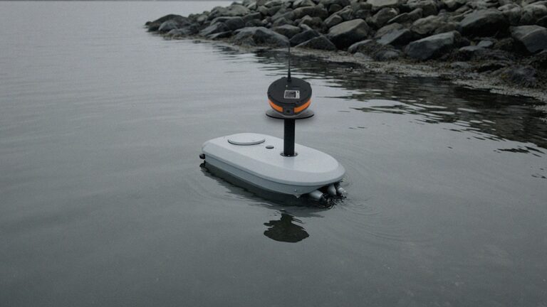 A small uncrewed survey catamaran with a repeater on a short mast, on calm coastal water